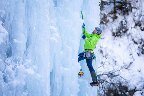 Ein Mann klettert mit dem Eiswerkzeug an einem Wasserfall empor. 