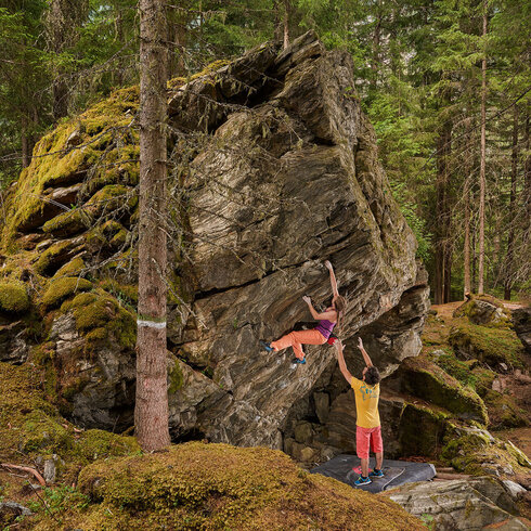 Two climbers bouldering in the shady forest. The boulder is certainly 4 meters high. Partner protection is also important when bouldering.