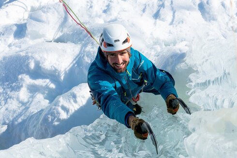 Ein freundliches Lächeln beim Eisklettern. Beide Eisgeräte sind fest ins Eis geschlagen worden.