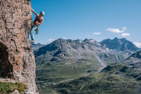 Frau klettert auf einem Felsen, mit Traumhafter Bergkulisse im Hintergrund.