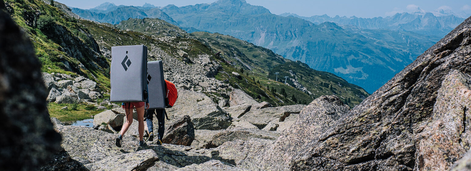 Zwei Personen gehen mit Ausrüstung auf einem Berg.