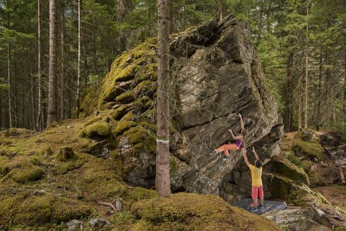 Ein Mann steht mit ausgestreckten Armen unter eine Frau, während diese auf einem Felsen klettert.