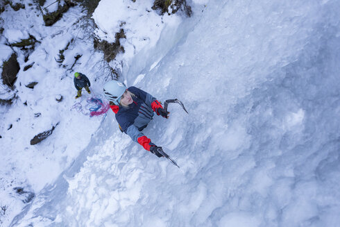 A woman climbs up the frozen waterfall with ice tools.