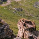 Das Bild zeigt den Hüttenblock bei der Heidelberger Hütte mit einer Klettererin darauf. Im Hintergrund grüne Wiesen.