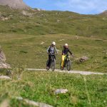 Das Bild zeigt zwei Radfahrer bei eBike and Climb zur Heidelberger Hütte. Seitlich des Schotterweges sieht man grüne Wisen.