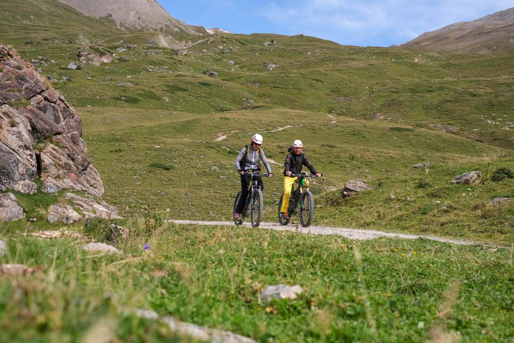 Das Bild zeigt zwei Radfahrer bei eBike and Climb zur Heidelberger Hütte. Seitlich des Schotterweges sieht man grüne Wisen.