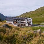 Das Bild zeigt die HEidelberger Hütte hinter einer grünen Wiese.